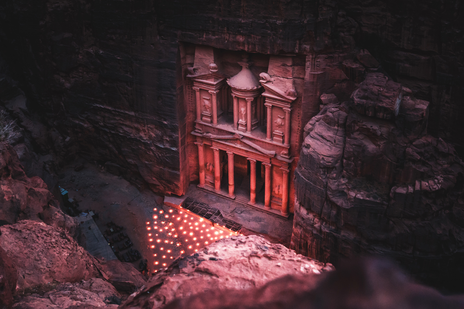 Ancient stone facade illuminated by soft lights, carved into a cliff, surrounded by dramatic rock formations, evoking a sense of historical grandeur and mystery at dusk.